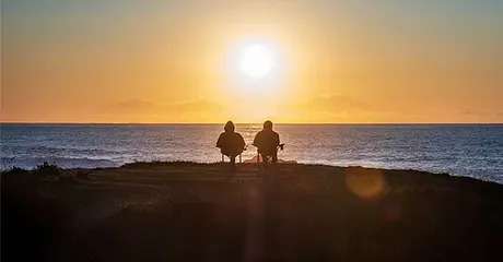 an elderly retired couple sitting on a beach watching the sun set listing.webp